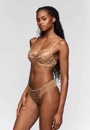 Beiges lingeriesetje van mesh, met een beha met een zigzag paillettenpatroon en een bijpassende doorschijnende string met uitsnijdingen.