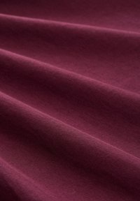 Le tissu en coton bordeaux présente une texture lisse avec de subtils plis, mettant en valeur une couleur riche et un motif de tissage uniforme.