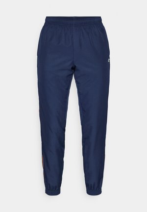 Marineblauwe sportbroek gemaakt van gladde stof, met een elastische tailleband, omgeslagen enkels en een klein logo aan de zijkant.