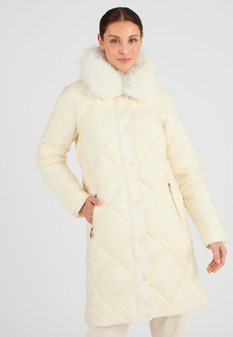 Cappotto invernale imbottito di colore crema, con un colletto in morbido pelliccia sintetica bianca, motivo a rombi e tasche laterali con zip.