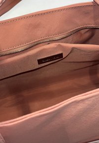 Wnętrze jasnoróżowej torby z kieszenią na zamek błyskawiczny oraz otwartą kieszenią z małą skórzaną metką marki wewnątrz.