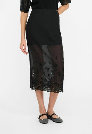 Schwarzer Rock mit einem opaken oberen Abschnitt und einem transparenten unteren Abschnitt, der aufwändige schwarze Paisley-Stickereien und einen gewellten Saum aufweist.