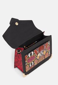 Sac à main synthétique noir avec un motif serpent rouge texturé à l'avant, des accents de quincaillerie dorée, et un design à rabat ouvert révélant un intérieur spacieux.