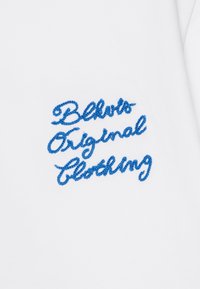 Balts audums ar zilu izšūtu tekstu: "Blvds Original Clothing," ar dekoratīvām kursīvā rakstāmajiem burtiem un teksturētu izšuvumu.
