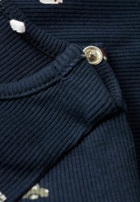 Marineblauwe geribde stof met een knoopdetail en een textuurrand. Voorzien van contrasterende witte en gekleurde motieven. Zacht, gestructureerd model.