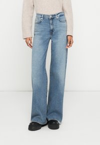 Jeans de ganga azul claro com perna larga e acabamento ligeiramente desbotado. Apresentam o clássico estilo de cinco bolsos e fecho de correr.