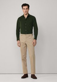 Ciemnozielona koszula z guzikami o gładkiej fakturze, w połączeniu z beżowymi spodniami. Koszula posiada kołnierzyk i guziki, a spodnie mają dopasowany krój.