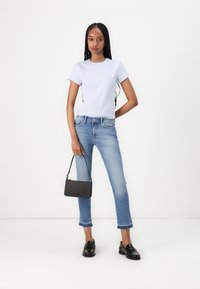 Svijetloplava majica s kratkim rukavima, svijetloplave skraćene traperice s poderanim rubom, crne ravne mokasine i crna pravokutna torba.