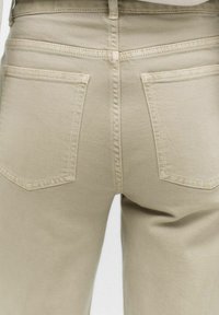 Beige denimbyxor med en klassisk design med fem fickor, synlig sömnad och en slät yta. Bakdelen har två påsydda fickor.