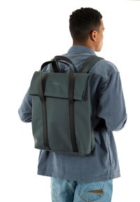 Mochila impermeable de color verde oscuro con cierre enrollable, correas negras y un diseño de marca mínima, creada para la funcionalidad y la durabilidad.