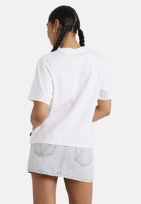 Witte katoenen T-shirt met korte mouwen, relaxte pasvorm en een rechte zoom, gecombineerd met een lichte spijkerrok met achterzakken.