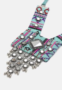 Barevný tkaný náhrdelník s tyrkysovou tkaninou, kovovými stříbrnými akcenty, reflexními kousky a ozdobným třásňovým okrajem z obecných prvků.