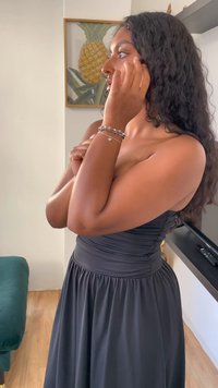 Abito nero senza spalline con dettagli di tessuto arricciato. Capelli in boccoli sciolti, adornati con un bracciale con accenti a forma di cuore e perle.