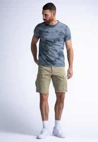 Šedá košile s krátkým rukávem a texturovaným vzorem, kombinovaná s khaki cargo šortkami s několika kapsami a bílými teniskami.