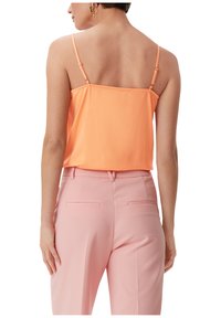 Brzoskwiniowa koszulka na ramiączkach z cienkimi paskami, gładką fakturą i luźnym krojem, w połączeniu z jasnoróżowymi spodniami typu tailored z tylnymi kieszeniami.