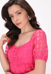 Pinkes Kleid mit Karomuster, kurzen Puffärmeln und gerafften Details am Ausschnitt. Silberschmuck ergänzt das Outfit.