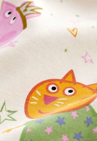 Tissu blanc présentant des visages d'animaux cartoon colorés, dont un personnage rose avec une couronne et un chat orange, entourés d'étoiles et de cœurs.