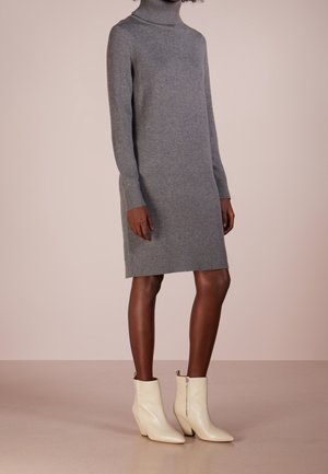 Persona que lleva un vestido jersey gris de manga larga y cuello alto, con puños y bajo acanalados, combinado con botines crema hasta el tobillo con cremalleras laterales.