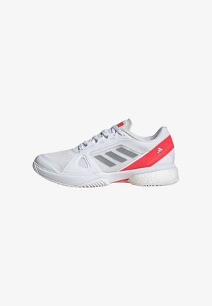 Chaussure de sport blanche avec des rayures grises, un accent rouge au talon et une semelle rembourrée, conçue pour le sport ou un usage décontracté.