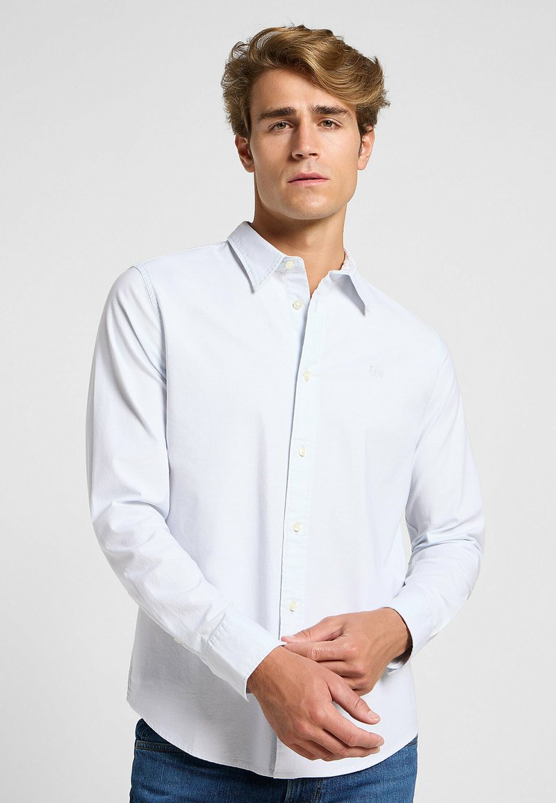 Camisa de botón de manga larga en azul claro, con cuello, hecha de algodón, que presenta un pequeño logo en el lado izquierdo del pecho y cierre de botones estándar.