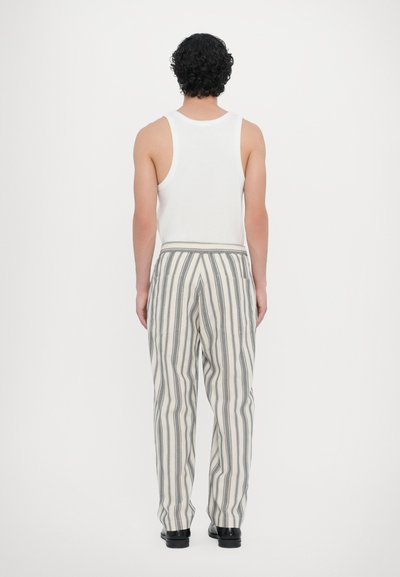 White tank top and striped pants with gray and cream colors. Pants feature a relaxed fit and an elastic waistband. Flat-sole shoes.