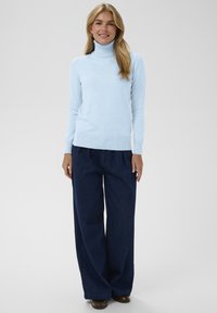 Ljust blått polokrage-sweater med långa ärmar och ribbad nederkant, i kombination med löst sittande mörkblå vida jeans.