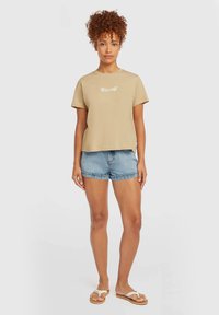 Beige cotton t-shirt with short sleeves and crew neck, featuring white floral embroidery; paired with denim shorts and sandals.