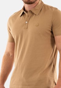 Polo a maniche corte in cotone beige, con colletto con bottoni, logo discreto sul petto e orlo dritto. Texture liscia.