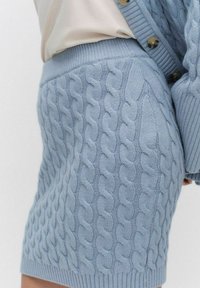 Vaaleansiniset neulotut shortsit, joissa on kaapeliteksti ja joustovyötärö sekä sivuyksityiskohtia. Kangas näyttää pehmeältä ja teksturoidulta.