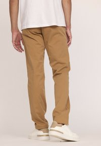 Pantalons en coton beige à coupe droite et texture lisse, associés à des baskets blanches avec des accents beiges.