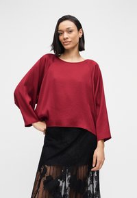 Haut bordeaux à manches longues en tissu lisse, avec un col arrondi et une coupe décontractée, associé à une jupe noire bordée de dentelle.