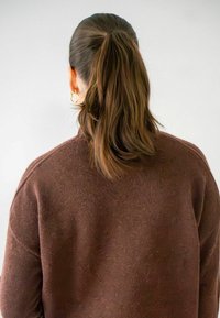 Pull en maille marron avec une coupe décontractée et un col haut, vu de dos, présentant des cheveux longs attachés enqueue de cheval. Pas de motifs ou d'accents visibles.