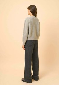 Pull en laine gris clair avec un col rond, coupe décontractée. Associé à un jean noir à taille haute et à jambes larges. Texture lisse.