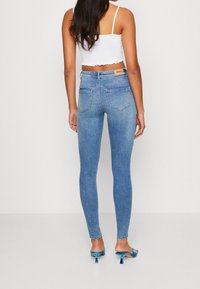 Tunna blå jeans med hög midja, blekt tvätt, och två bakfickor. Bärs med en vit croppad linne och blå klackar.