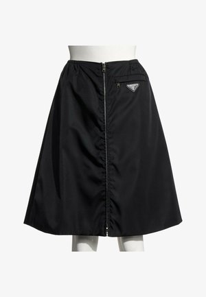 Jupe noire en forme trapèze avec fermeture éclair devant et petite poche zippée avec le logo Prada sur le côté droit de la ceinture.