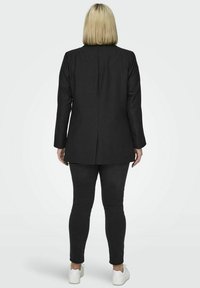 Črn blazer s strukturiranim dizajnom, z enim zadnjim razporkom, v kombinaciji s ozkimi črnimi jeans hlačami in belimi supergami, kar prikazuje čist in sodoben videz.