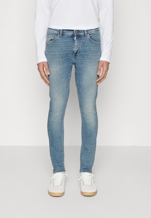 Světle modré džíny slim fit, vyrobené z denimu, s jemným vyblednutím, klasickým pětipocketovým designem a zapínáním na zip. Bílá sportovní obuv dokončuje vzhled.
