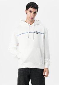 Witte hoodie met een voorste kangoeroezak, grijze trekkoorden en een logo met een marineblauwe streep over de borst.