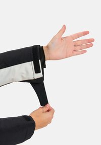Manica di giacca bianca e nera con un cinturino in Velcro che tiene fermo il polsino. Mano mostrata in posizione aperta, per evidenziare il design e la texture della manica.