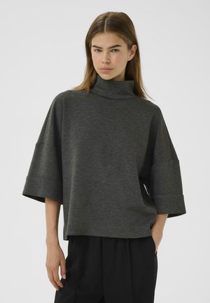 Haut surdimensionné gris foncé avec un col montant, des épaules tombantes et des poignets retroussés, fabriqué dans un tissu doux, avec une texture lisse.
