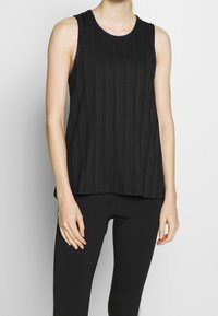 Haut sans manches noir avec une texture à côtes verticales, encolure ronde et bordures scintillantes. Associé à un legging noir.