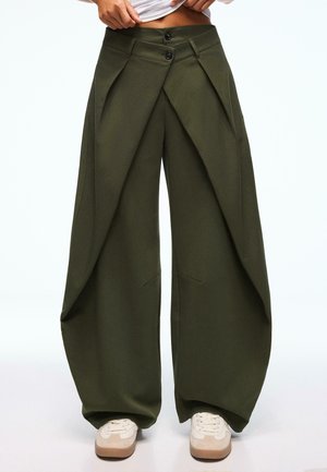 Wide-leg olive green pants with a unique overlapping design, featuring two front buttons and side pockets. Smooth fabric and ample drape.