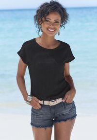 Schwarzes, strukturiertes T-Shirt mit kurzen Ärmeln, kombiniert mit dunkelblauen Jeansshorts mit ausgefranstem Saum. Accessoires umfassen einen beigen Gürtel und mehrfarbige Armbänder.