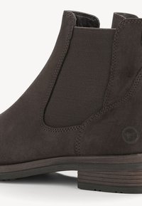 Botte Chelsea en daim brun foncé avec panneau latéral élastique, talon bas empilé et logo embossé discret près du talon.