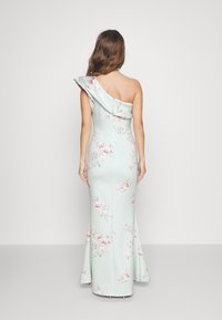 Yksi olkaimellinen kukkamekko vaalean mintunvihreästä kankaasta, jossa on rypytetty kaula-aukko, pinkkejä kukkakuoseja ja levenevä helma.