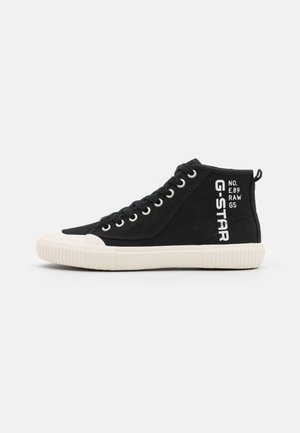 Czarny tenisówka typu high-top z płótna z białą gumową podeszwą, białym noskiem, metalowymi przelotkami i tekstowym logo G-STAR po boku.