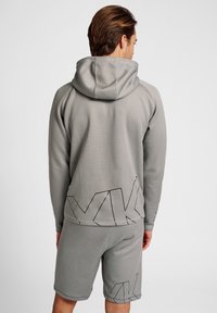 Sweatshirt gris à capuche avec un design simple et des accents géométriques noirs à l'arrière, associé à un short assorti de la même couleur et texture.