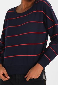 Sudadera de manga larga en color azul marino con rayas horizontales rojas, escote redondo, puños y dobladillo acanalados. Tejido suave con un corte relajado.