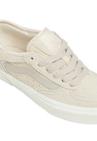 Beige mockasinhandske med en texturerad yta, som har en slät läder sida, platta snörningar och en vit gummisula.