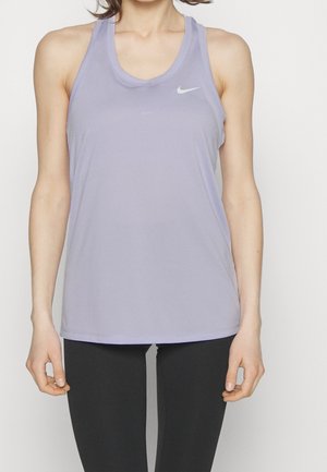 Kvinde iført en lyse lilla Nike tanktop og sorte leggings står mod en ensfarvet baggrund.